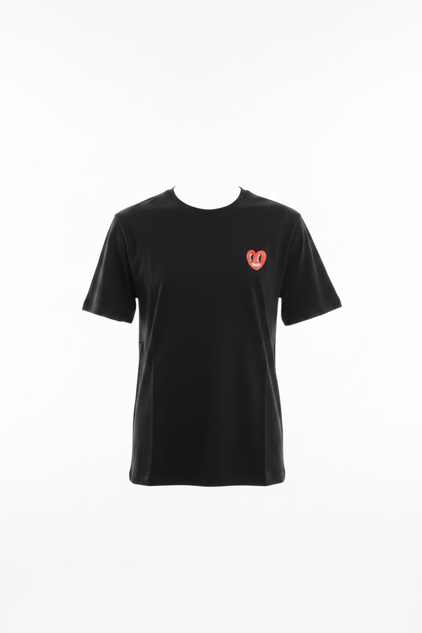 A black short-sleeve t-shirt with a red and white heart logo on the left chest, held up on a blue hanger by a hand in a warehouse or retail setting.